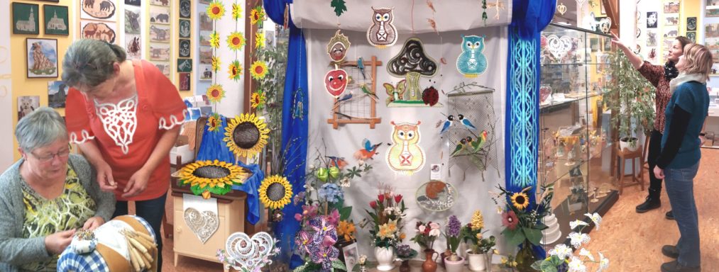 Zwei Personen betrachten Handarbeiten in einem bunten Ausstellungsraum. Hintergrund mit Dekorationen.