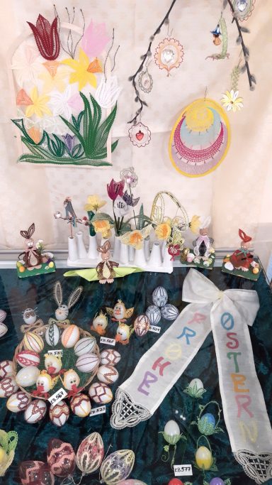 Bunte Ostereier und Dekorationen auf einem Tisch, umgeben von frühlingshaften Blumen.